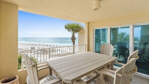 Un balcón con mesa y sillas de madera, vista a la playa y una palmera.