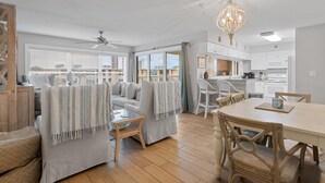 A spacious living room with a sofa, chairs, and a dining table. There is a kitchen area with cabinets and a microwave. - Beach-side, beautiful low-rise with uncrowded beach! (Destin)