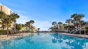 A swimming pool with lounge chairs and palm trees, surrounded by buildings. - Beach-side, beautiful low-rise with uncrowded beach! (Destin)
