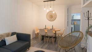 Moderni olohuone, jossa on sohva, ruokapöytä tuoleineen, riippuvalaisin ja rottinkituoli.