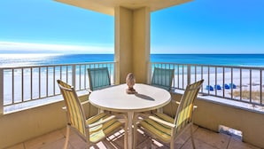 A balcony with a round table and chairs, overlooking a beach with a clear view of the ocean.