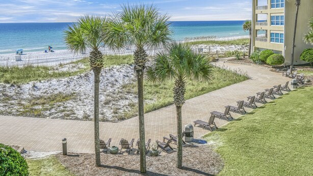 A beachside hotel with a paved walkway, palm trees, and beach chairs. - Beach-side, beautiful low-rise with uncrowded beach! (Destin)