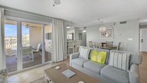 A living room with a sofa, a coffee table, and a laptop. There is a sliding glass door leading to a balcony with a table and chairs. - Beach-side, beautiful low-rise with uncrowded beach! (Destin)