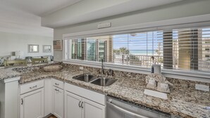 A kitchen with granite countertops, stainless steel sinks, and a view of the ocean through large windows. - Beach-side, beautiful low-rise with uncrowded beach! (Destin)