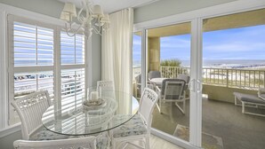 A balcony with a glass table and chairs, a view of the beach, and a hanging light fixture.