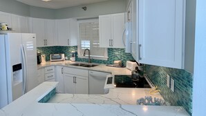 A modern kitchen with white cabinets, a marble countertop, and a green-tiled backsplash.