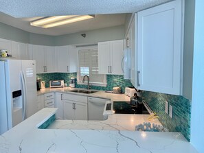 A modern kitchen with white cabinets, a marble countertop, and a green-tiled backsplash.