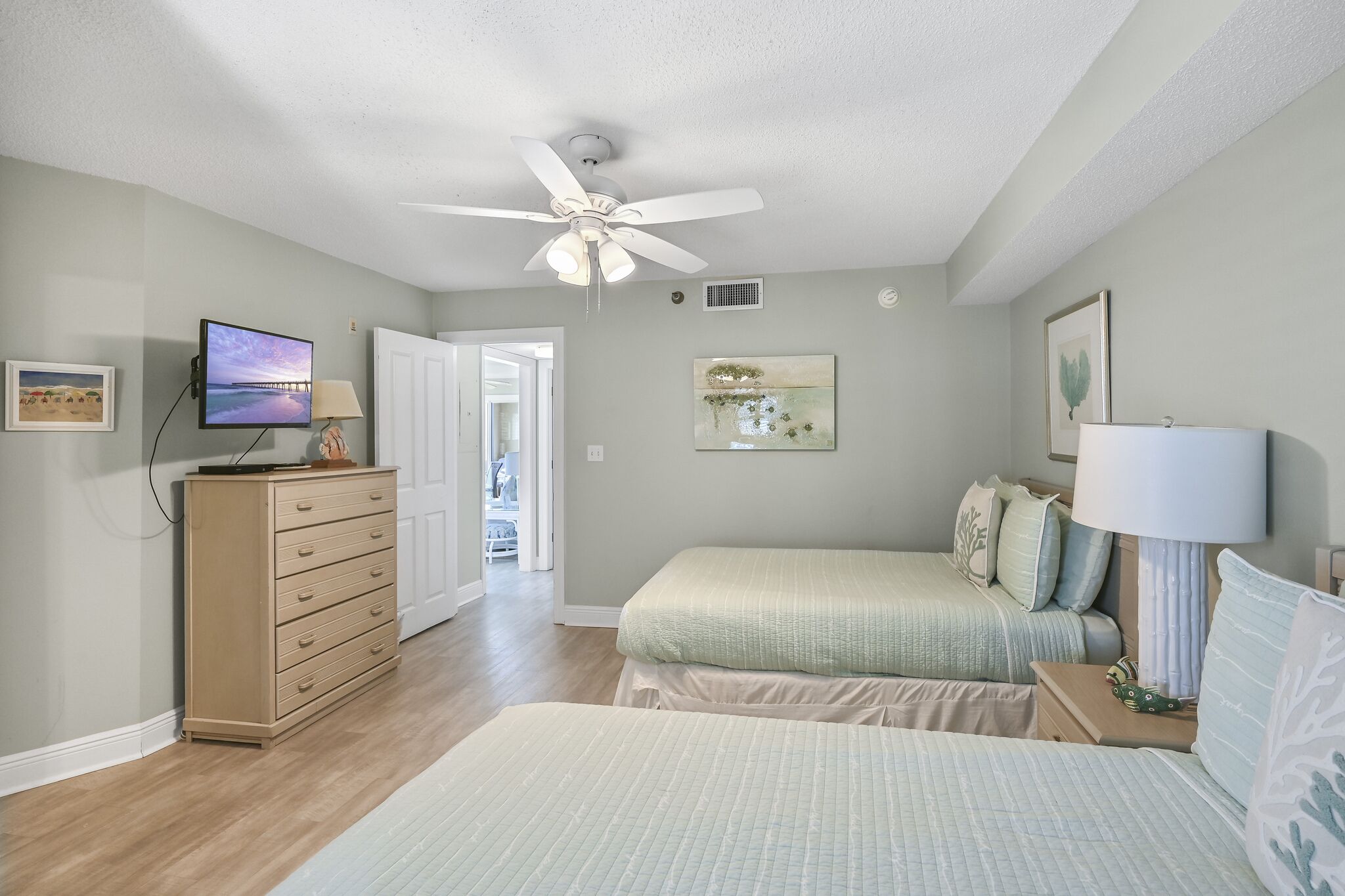 A bedroom with two beds, a ceiling fan, a TV, and artwork on the walls.