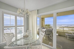 A balcony with a glass table and chairs, a view of the beach, and a hanging light fixture.