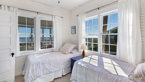 Une chambre avec deux lits, un ventilateur de plafond et de grandes fenêtres avec des rideaux.