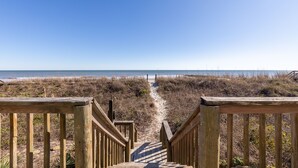 Un escalier en bois menant à une plage, avec un ciel dégagé.
