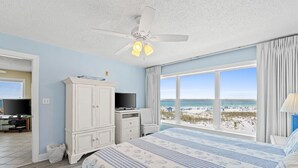 Une chambre avec un grand lit, un ventilateur de plafond, une télévision et une vue sur la plage.