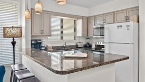 A kitchen with a granite countertop, stainless steel appliances, and light wood cabinets.
