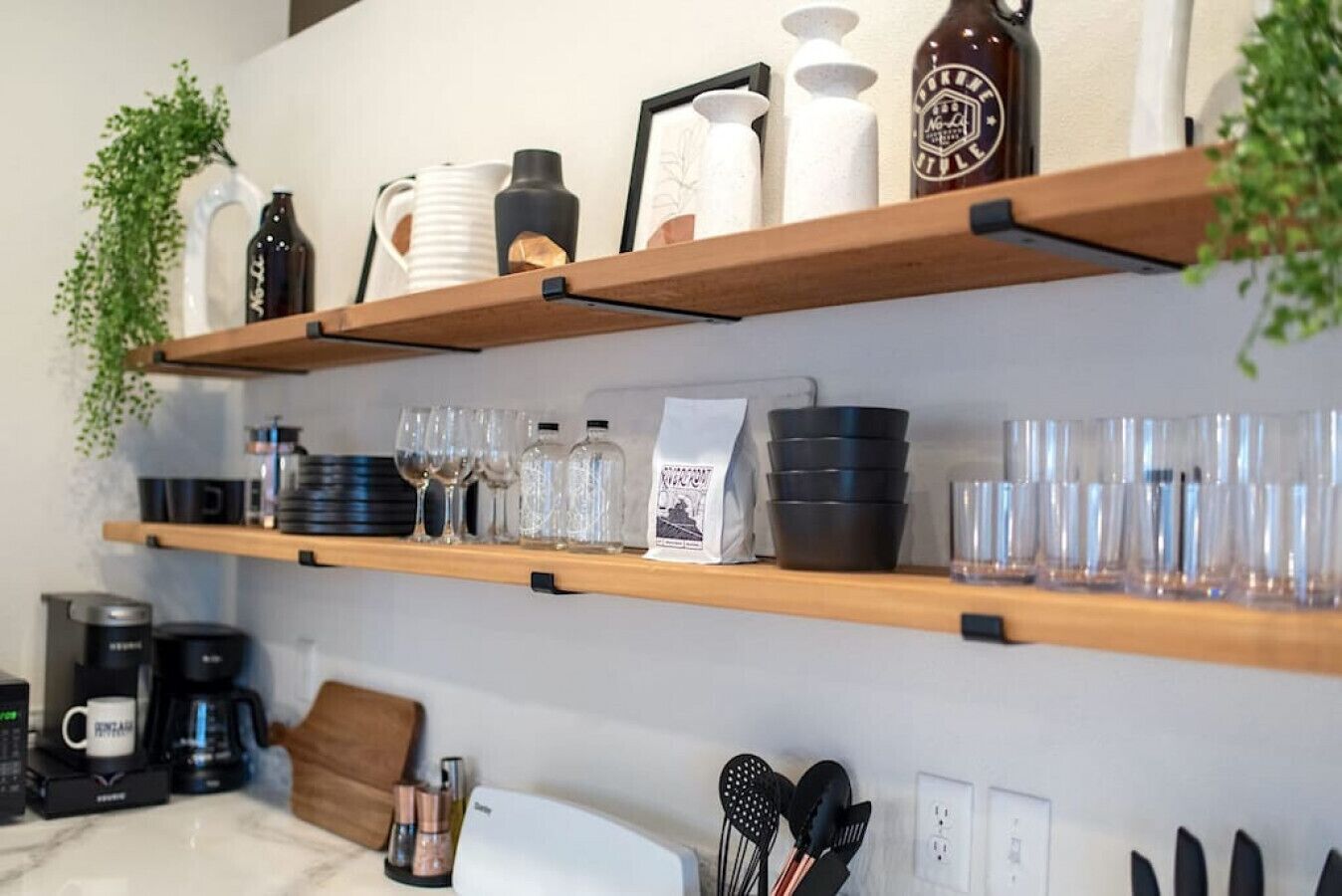 A kitchen with wooden shelves holding various glassware, a coffee maker, and a plant.