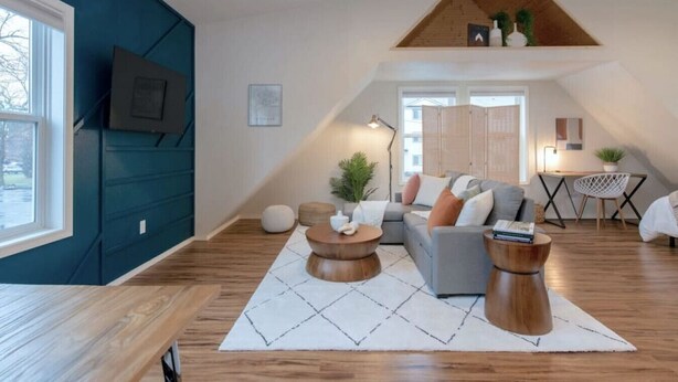 A modern loft apartment with a high ceiling, wooden flooring, and a mix of seating areas including a sofa and round tables. - U-District Loft near GU w/ Self Check-in & Wifi! (Spokane)