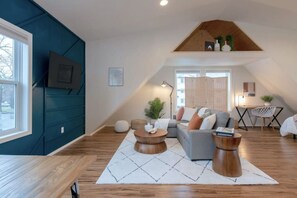 A modern loft apartment with a high ceiling, wooden flooring, and a mix of seating areas including a sofa and round tables. - U-District Loft near GU w/ Self Check-in & Wifi! (Spokane)
