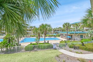 A hotel with a swimming pool surrounded by palm trees and a fenced area. - Beach-side, beautiful low-rise with uncrowded beach! (Destin)