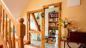 A wooden staircase with a heart-shaped mirror, a bookshelf with books and decorative items, and a radio on a table. - FW Gartenblick (Tanne)