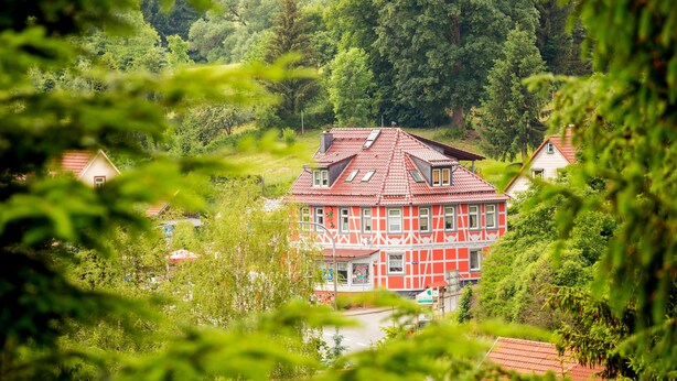 A red and white building with a sloped roof, surrounded by lush greenery. - FW Gartenblick (Tanne)