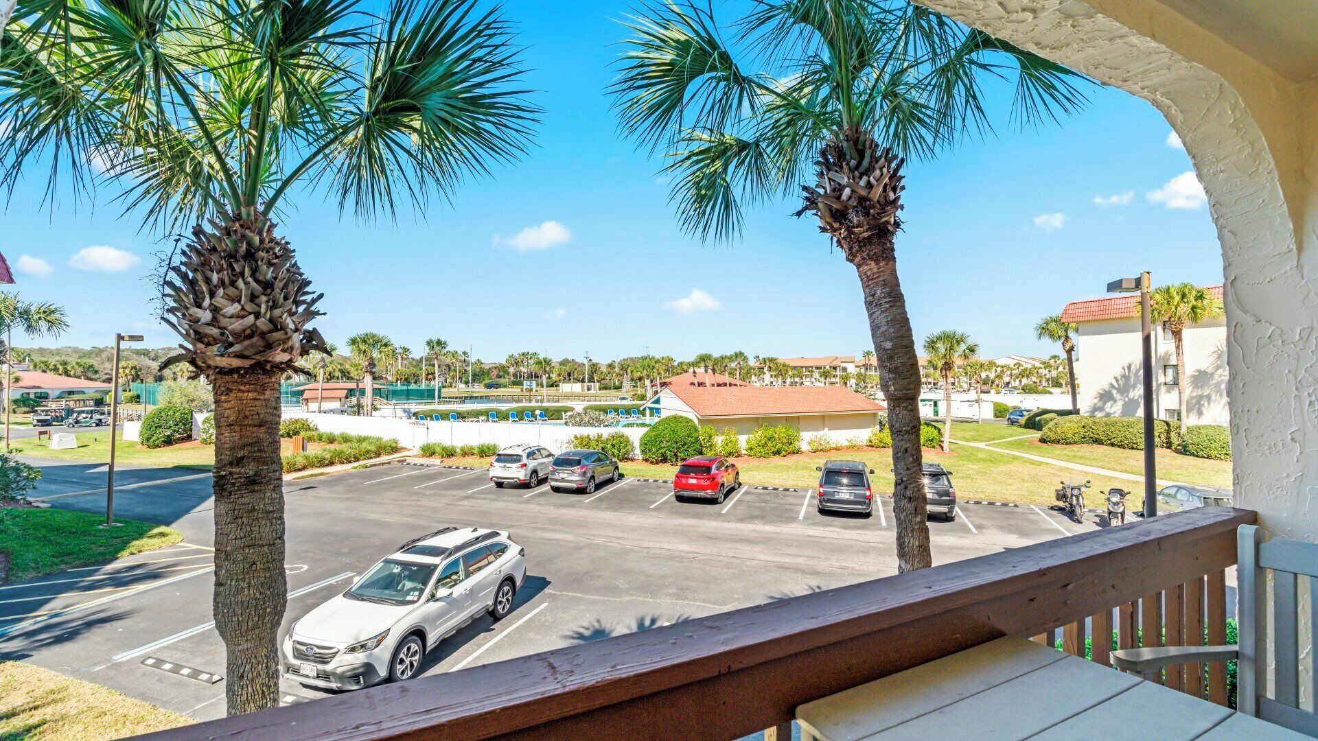 A parking lot with several cars, palm trees, and buildings in the background.