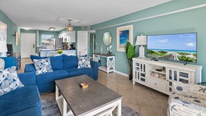A living room with a blue sofa, a coffee table, and a TV on a white stand. - Newly updated!! 2 Bed 2 Bath overlooking the pool and courtyard. (Destin)