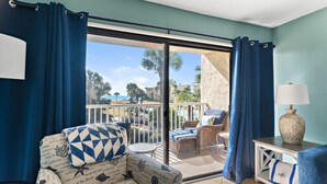 A room with a view of a balcony, a sofa with patterned upholstery, a small round table, and a lamp on a side table. - Newly updated!! 2 Bed 2 Bath overlooking the pool and courtyard. (Destin)