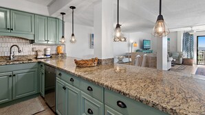 A kitchen with green cabinets, granite countertops, and pendant lighting. - Beach-side, beautiful low-rise with uncrowded beach! (Destin)