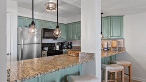 A kitchen with teal cabinets, a stainless steel refrigerator, a granite countertop, and two wooden stools. - Beach-side, beautiful low-rise with uncrowded beach! (Destin)