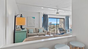 A modern living room with a sofa, a coffee table, and a bar area with stools. - Beach-side, beautiful low-rise with uncrowded beach! (Destin)