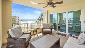 Ein Balkon mit Korbmöbeln, einem Deckenventilator und Blick auf den Strand.