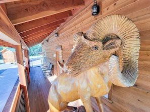 A wooden cabin with a large carved ram sculpture on the porch.