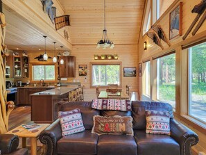 A cabin interior with a wooden ceiling, a dining area, a kitchen, and large windows. - Nordic Village Cabin in the heart of Mazama (Mazama)