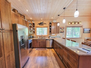 A modern kitchen with wooden cabinets, stainless steel appliances, and a large window. - Nordic Village Cabin in the heart of Mazama (Mazama)