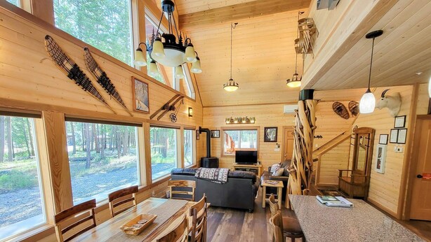 L’intérieur d’un chalet en bois comprend un coin repas, des sièges, un téléviseur et de grandes fenêtres.