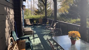 Une terrasse extérieure couverte, dotée d’un plancher en bois, de chaises en métal, d’une table et d’une plante en pot.