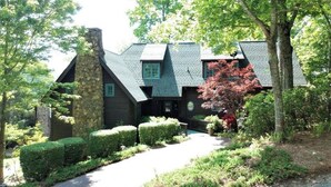 Un chalet rustique doté d’une cheminée en pierre, entouré de haies et d’arbres bien entretenus.