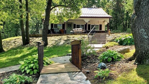 A house with a covered porch, a stone pathway leading to the entrance, and a small garden area with various plants.