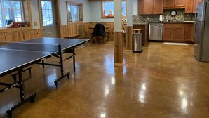 A spacious kitchen with wooden cabinets, a stainless steel refrigerator, and a ping pong table in the center.