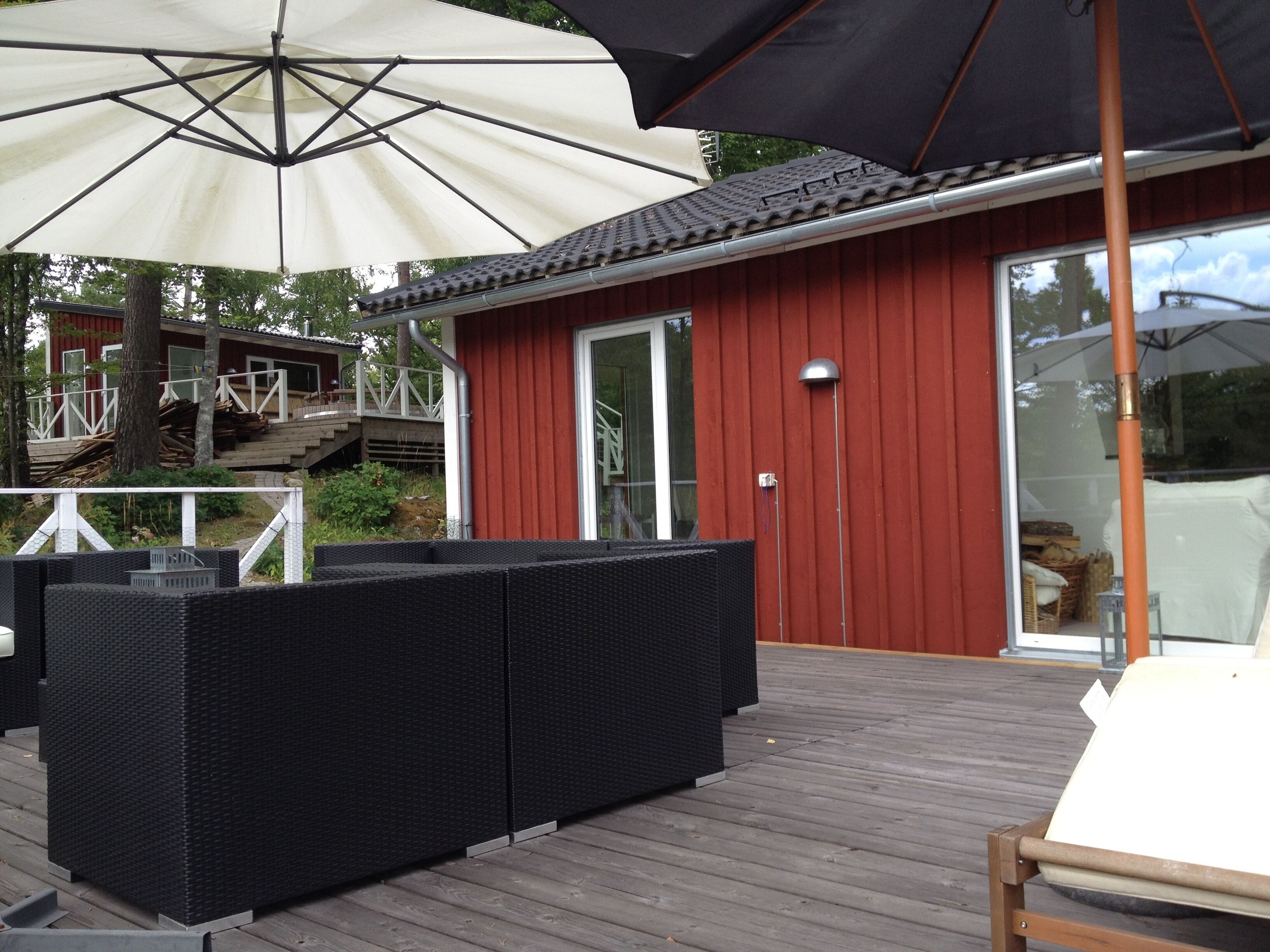A wooden deck with outdoor furniture, a red building with a glass door, and a white umbrella.