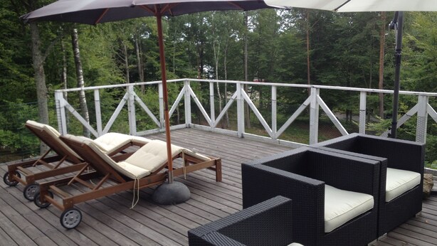Una terraza con mobiliario exterior, incluyendo sillones de descanso y un sofá, rodeada por una barandilla blanca.