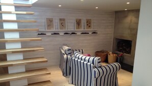 Un interior moderno con una escalera de madera, sofás a rayas, una chimenea y obras de arte en la pared.