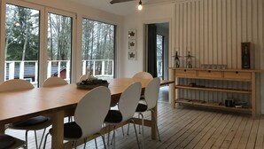 Un comedor moderno con una mesa y sillas de madera, ventanas amplias con vistas a árboles y un techo rústico con vigas a la vista.