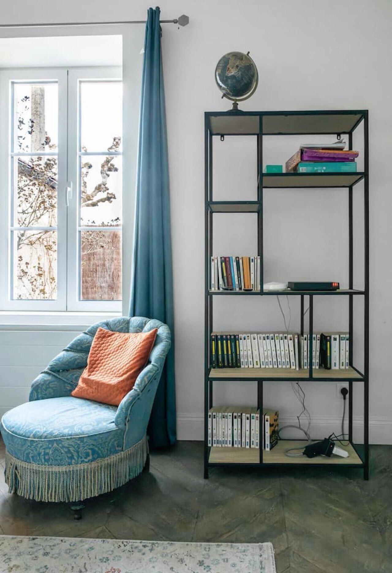 A room with a blue armchair, a bookshelf, and a globe on the wall.