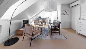 A modern loft bedroom with a sloped ceiling, a dining area with wicker chairs, a sofa, and a hanging light fixture.
