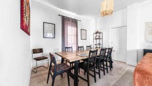 A dining area with a wooden table and chairs, a hanging light fixture, and a red tapestry on the wall.