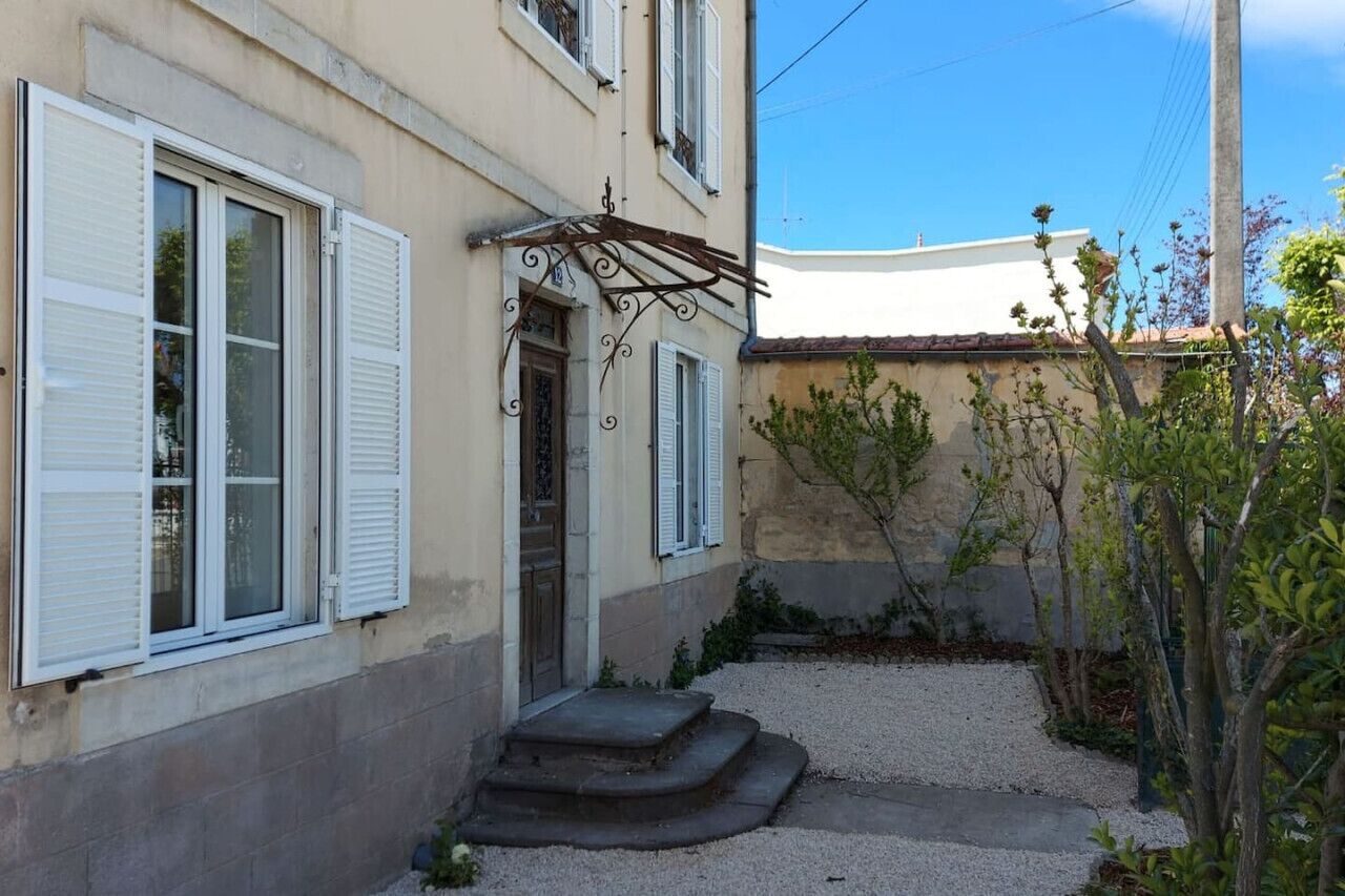 A building with white shutters, a door, and a small garden area with steps leading to the entrance.