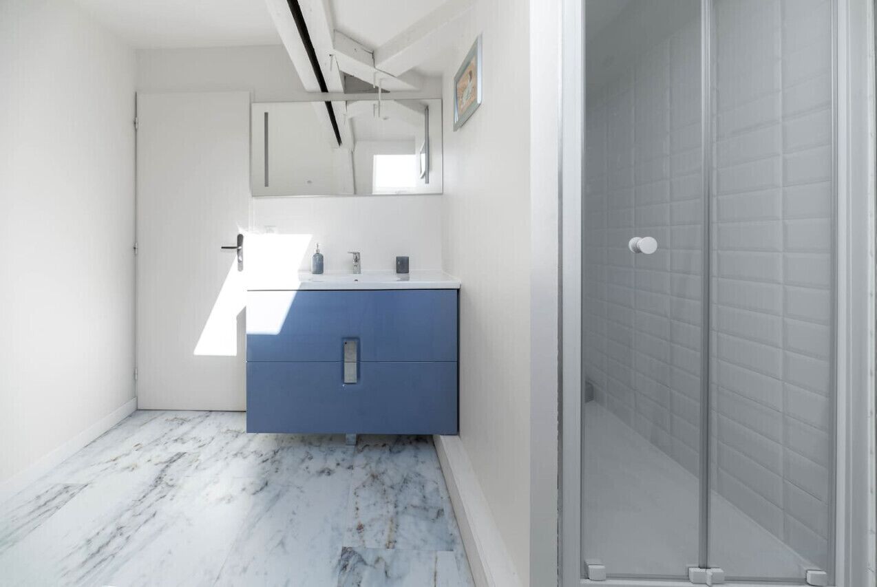 Ein Badezimmer mit Marmorboden, einem blauen Schrank, einem Spiegel und einer Duschkabine aus Glas.