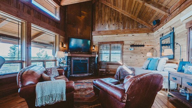 A cozy log cabin interior with a fireplace, leather sofas, and a television. - The Retreat at Rusty Elk Lodge, Star Valley Wyoming (Thayne)