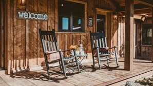 A wooden cabin with a 'welcome' sign, two rocking chairs, and a small table with a lantern. - The Retreat at Rusty Elk Lodge, Star Valley Wyoming (Thayne)
