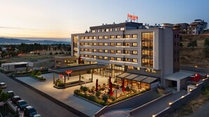 Un hotel moderno con varios pisos, un área exterior cubierta con asientos y un estacionamiento.